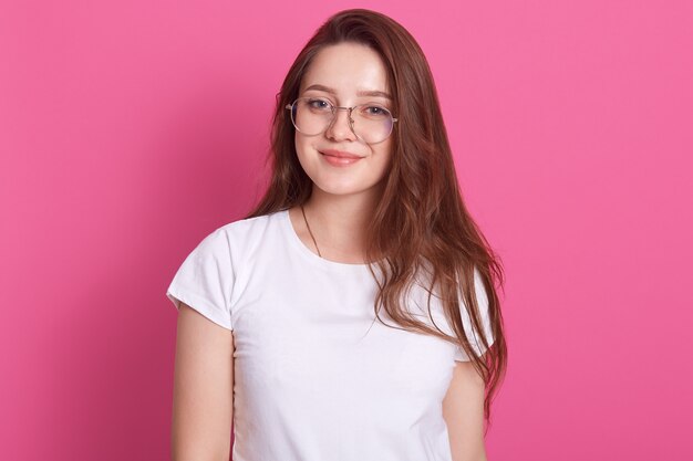 Entspannte sorglos lächelnde junge Frau, die weißes lässiges T-Shirt und Brille trägt und positiven Gesichtsausdruck hat