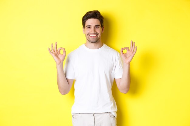 Entspannter Kerl, der lächelt, okayzeichen zeigt, zustimmt oder zustimmt, vor gelbem Hintergrund stehend