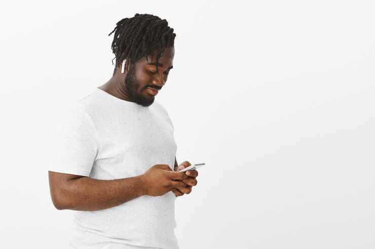 Kostenlose Foto entspannter kerl mit zöpfen, der mit seinem telefon gegen die weiße wand posiert