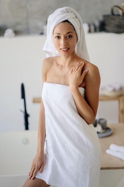 Entspanntes junges kaukasisches weibliches Modell im weißen Handtuch, fühlt sich nach dem Duschen erfrischt an, hat gesunde, saubere, weiche Haut, posiert im gemütlichen Badezimmer. Frauen-, Schönheits- und Hygienekonzept.