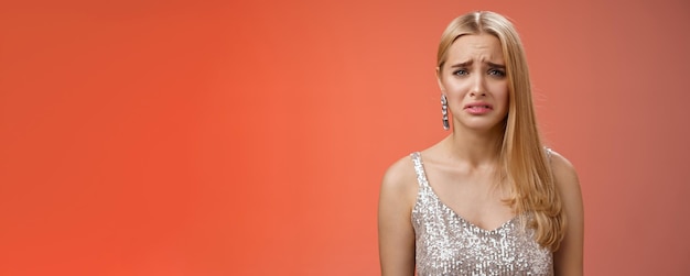 Kostenloses Foto enttäuscht, sich beschwerend, süße blonde frau in silbernem, stylischem kleid, die das gesicht verzieht und die stirn runzelt, ist schlecht