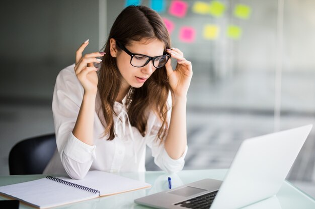 Enttäuschte Geschäftsfrau, die in ihrem Büro in weißen Kleidern am Laptop arbeitet