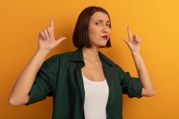 Enttäuschte hübsche Frau zeigt mit zwei Händen auf orange Wand isoliert