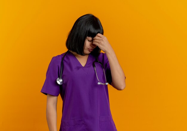 Enttäuschte junge brünette Ärztin in Uniform mit Stethoskop legt Hand auf die Stirn