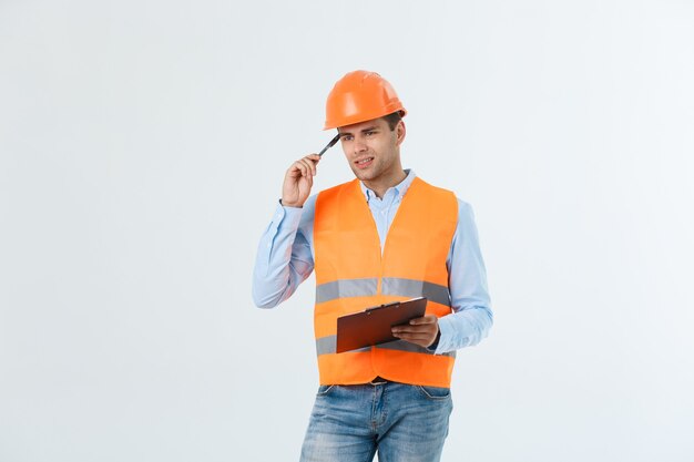 Enttäuschter, gutaussehender Ingenieur mit orangefarbener Weste und Jeans mit Helm, isoliert auf weißem Hintergrund.