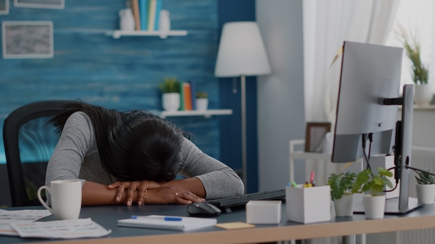 Enttäuschter Workaholic-Student, der auf Schreibtischtisch im Wohnzimmer schläft, nachdem er zum Termin des Jobprojekts von zu Hause aus gearbeitet hat