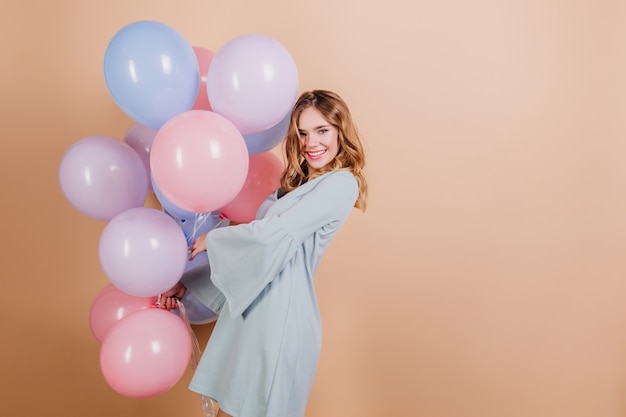 Entzückende blonde weiße Frau in der blauen Kleidung, die mit schönen Luftballons aufwirft