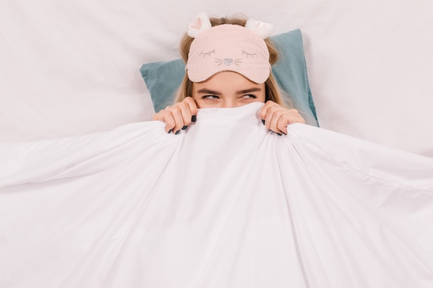 Entzückende Frau in der Schlafmaske, die im Bett aufwirft