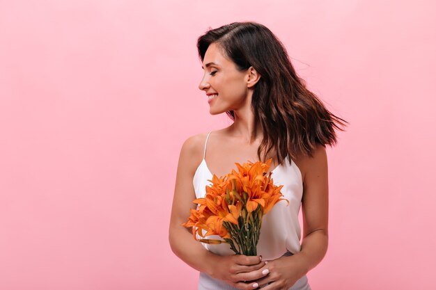 Entzückende Frau in der Spitze lacht und wirft mit Blumenstrauß auf rosa Hintergrund auf