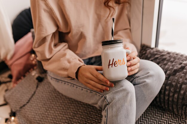 Entzückende Frau in lässiger Kleidung, die in ihrem Zimmer mit Tasse Tee sitzt. Bezauberndes Mädchen, das Glühwein im Winter genießt.