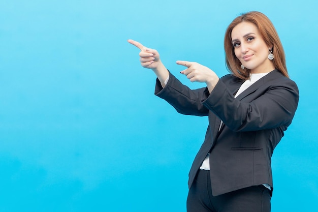 Entzückende Geschäftsfrau, die auf blauem Hintergrund steht und ihre Finger beiseite zeigt