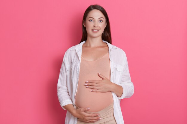 Entzückende glückliche junge schwangere Frau, die ihren Bauch berührt