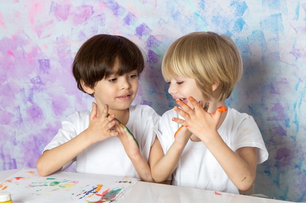 Entzückende Kinder in den weißen T-Shirts, die mit bunten Farben spielen