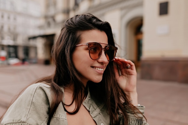 Entzückende schöne Frau mit langen dunklen Haaren in brauner Brille mit wunderbarem Lächeln schaut zur Seite