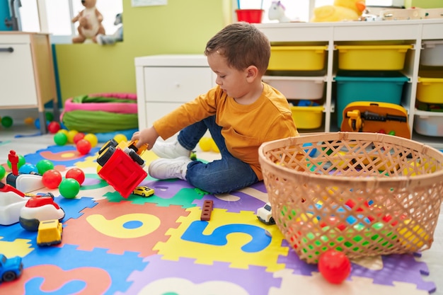 Entzückender kaukasischer Junge, der mit Traktorspielzeug spielt, das im Kindergarten auf dem Boden sitzt