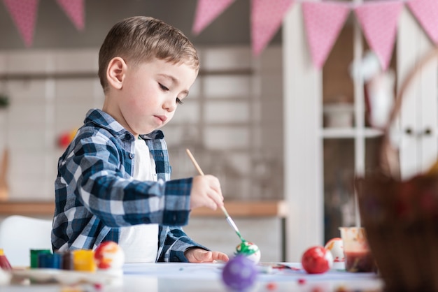 Entzückender kleiner Junge, der Eier für Ostern malt