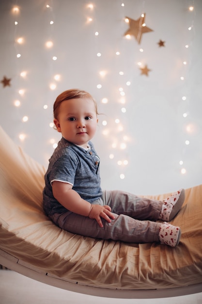 Entzückendes Baby, das auf schöner Schaukel sitzt, die für Weihnachten verziert wird.