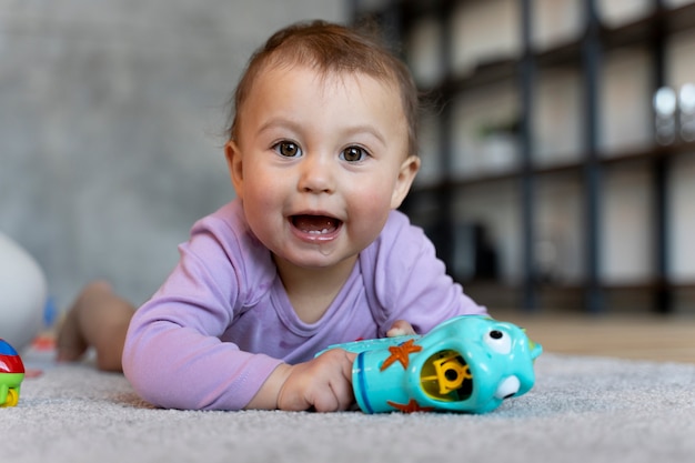 Entzückendes Baby, das mit Spielzeug auf dem Boden liegt und spielt