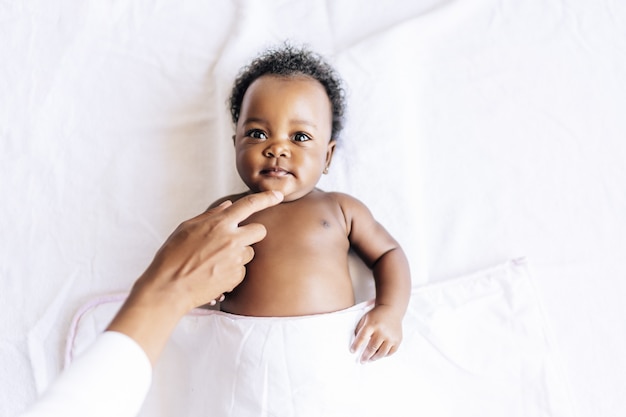 Entzückendes fröhliches afroamerikanisches Baby, das im Bett liegt