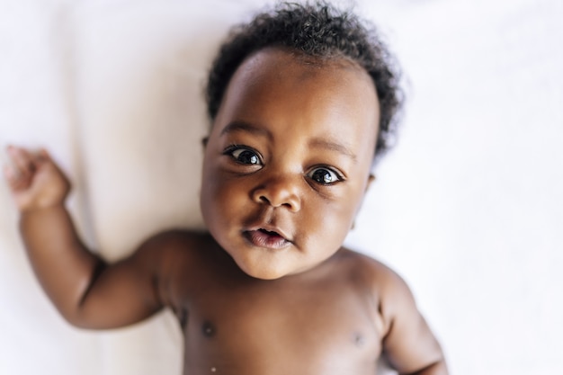 Entzückendes fröhliches afroamerikanisches Baby, das im Bett liegt
