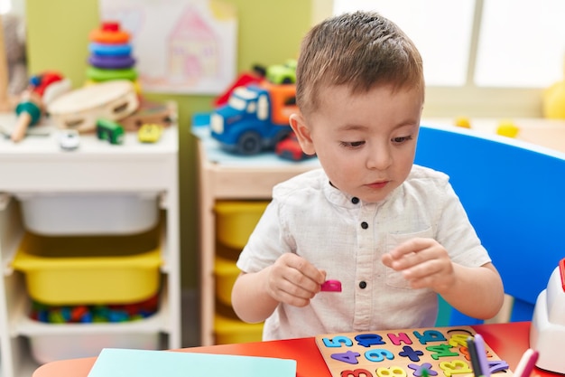 Kostenloses Foto entzückendes hispanisches kleinkind, das mit einem mathe-puzzle-spiel spielt, das im kindergarten auf dem tisch sitzt
