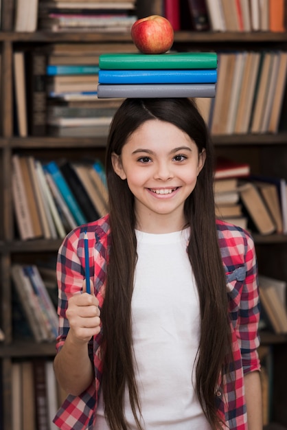 Entzückendes junges Mädchen, das Bücher auf ihrem Kopf hält