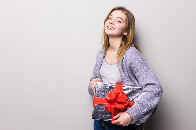 Entzückendes junges Mädchen, das Kasten mit Geschenk lokalisiert auf Weiß betrachtet