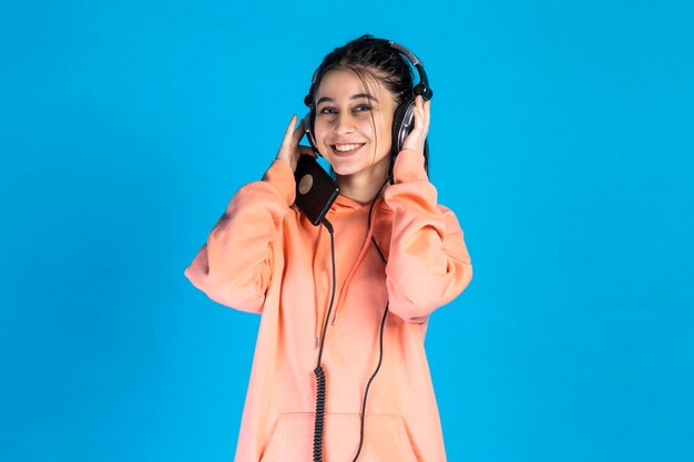 Entzückendes junges Mädchen, das lächelt und Musik auf ihren Kopfhörern hört Foto in hoher Qualität