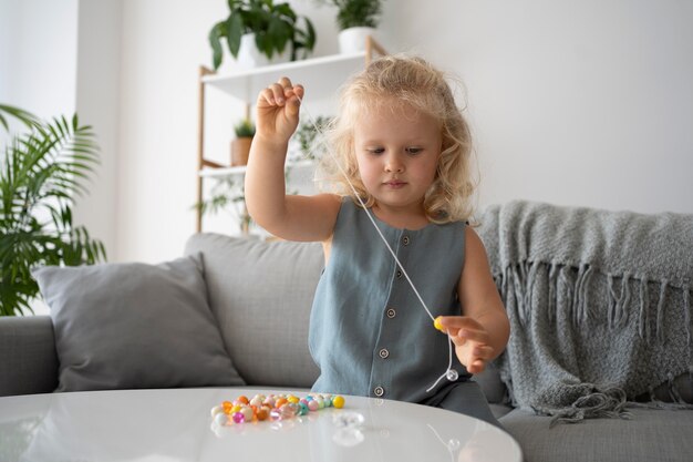 Entzückendes kleines Mädchen, das Accessoires mit verschiedenen bunten Bällen herstellt