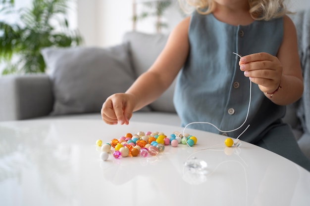 Entzückendes kleines Mädchen, das Accessoires mit verschiedenen bunten Bällen herstellt