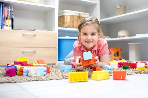 Entzückendes kleines Mädchen, das auf dem Teppich liegt und mit kleinen bunten Spielsachen spielt