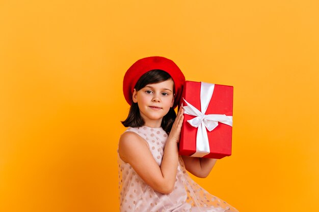 Entzückendes kleines Mädchen im Kleid, das Geburtstagsgeschenk hält. Kind erraten, was in Geschenk.