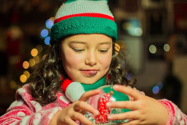 Entzückendes Mädchen, das ihre Weihnachtsglaskugel hält und betrachtet