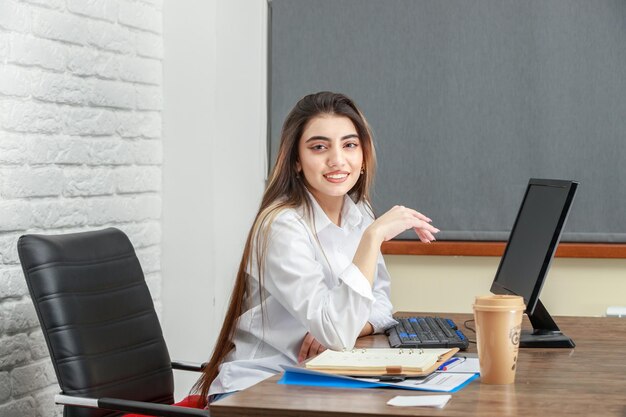 Entzückendes Mädchen, das im Büro sitzt und lächelt Hochwertiges Foto