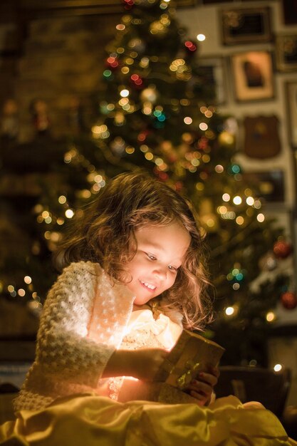 Entzückendes Mädchen, das lächelt und ihr Weihnachtsgeschenk betrachtet