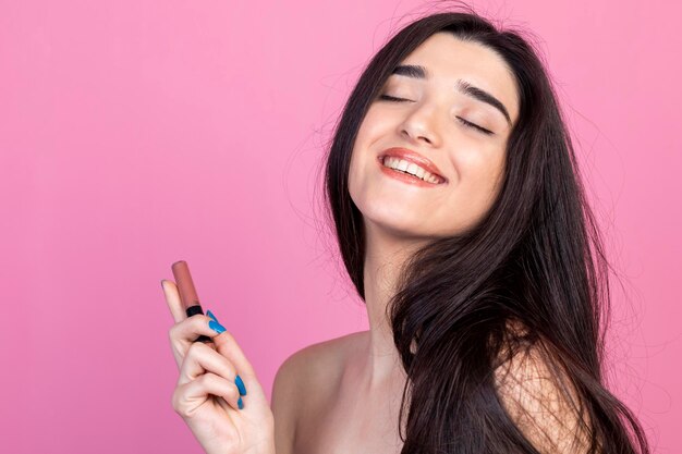 Entzückendes Mädchen, das Lippenstift hält und auf rosa Hintergrund lächelt Hochwertiges Foto