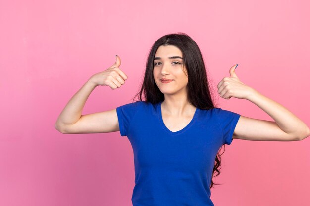 Entzückendes Mädchen Geste Daumen hoch und stehend auf rosa Hintergrund Hochwertiges Foto