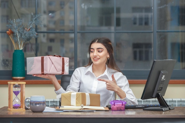 Entzückendes Mädchen mit Geschenkbox und Pint-Finger darauf im Büro Foto in hoher Qualität