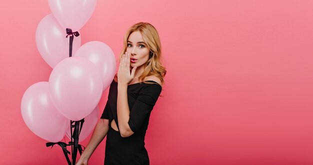 Entzückendes romantisches Geburtstagskind, das Erstaunen ausdrückt. Foto der gutaussehenden jungen Frau mit der hübschen Frisur, die mit Luftballons aufwirft.