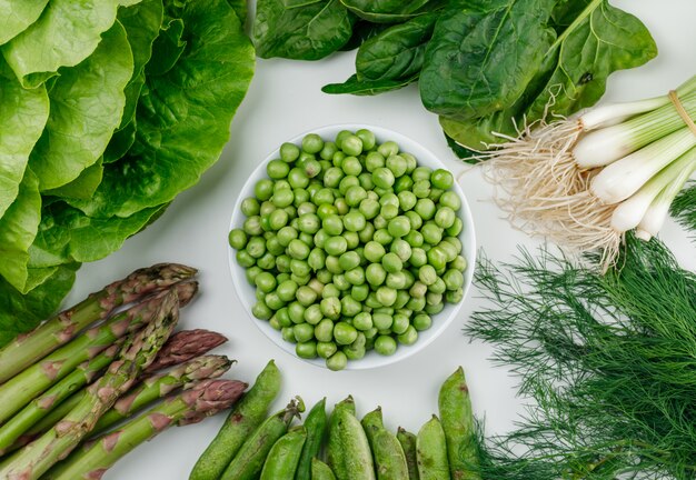 Erbsen mit Salat, Spargel, grünen Schoten und Zwiebeln, Dill, Sauerampfer in einer weißen Schüssel auf weißer Wand, Draufsicht.