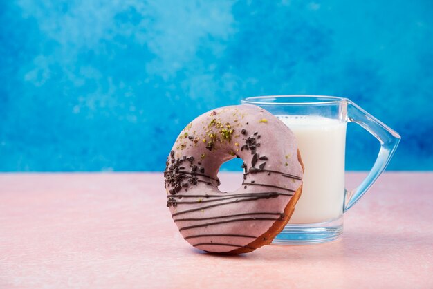 Erdbeer Donut mit Dekorationen und einem Glas Milch auf rosa Tisch.