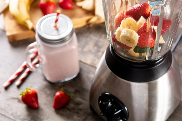 Erdbeer- und Bananen-Smoothie im Mixer auf Holztisch zubereiten