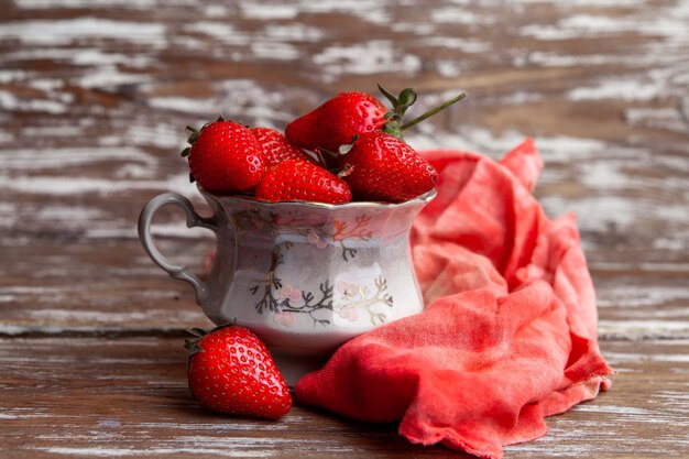 Erdbeeren der Seitenansicht in einer Kaffeetasse mit rotem Tuch auf hölzernem Hintergrund. horizontal