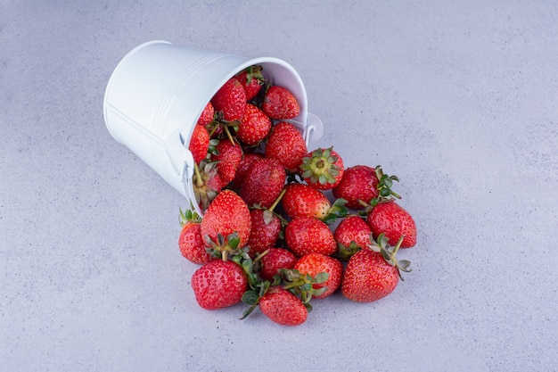 Erdbeeren, die aus einem kleinen Eimer auf Marmorhintergrund gießen. Foto in hoher Qualität