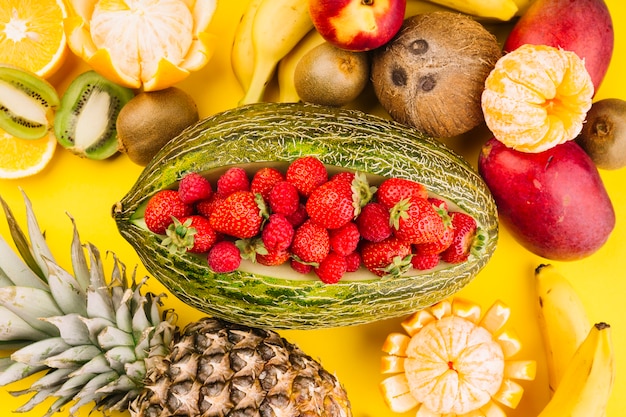 Kostenloses Foto erdbeeren in der grünen netto-melone mit kokosnuss; kiwi; mango; banane; ananas und orangen auf gelbem grund