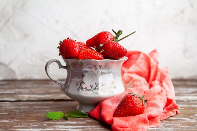 Erdbeeren in einer Kaffeetasse mit roter Stoffseitenansicht auf einem hölzernen und weißen Hintergrundraum für Text