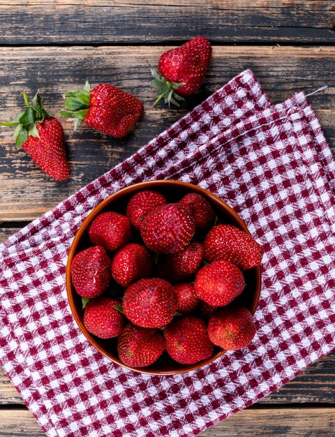 Erdbeeren in einer Schüssel auf einem Picknicktuch und einem Holztisch. Draufsicht.