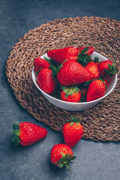 Erdbeeren in einer Schüssel hohen Winkelansicht auf einem Untersetzer und grau strukturiertem Hintergrund