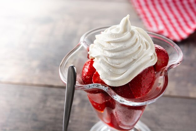 Erdbeeren und Schlagsahne im Eisglas auf Holztisch