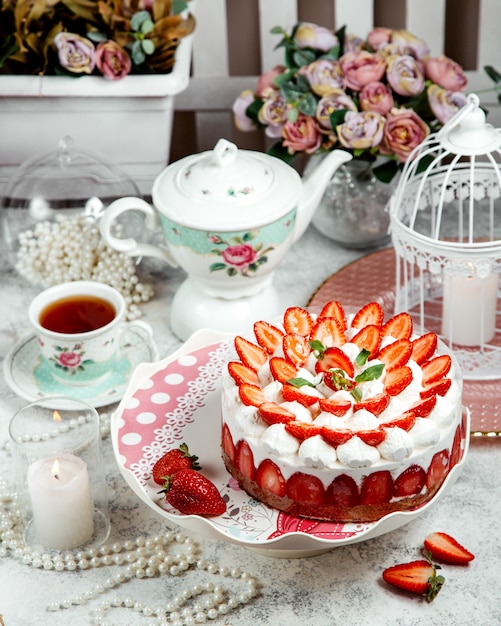 Erdbeerkuchen verziert mit geschnittenen Erdbeeren und einem schwarzen Tee